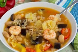 Auf dem Bild ist ein bunter Garnelen-Spitzkohltopf mit Reis zu sehen. Das ist ein Eintopf mit Reis und dicken weißen Bohnen, Garnelen, viel gelber und roter Paprika, Aubergine und Spitzkohl.